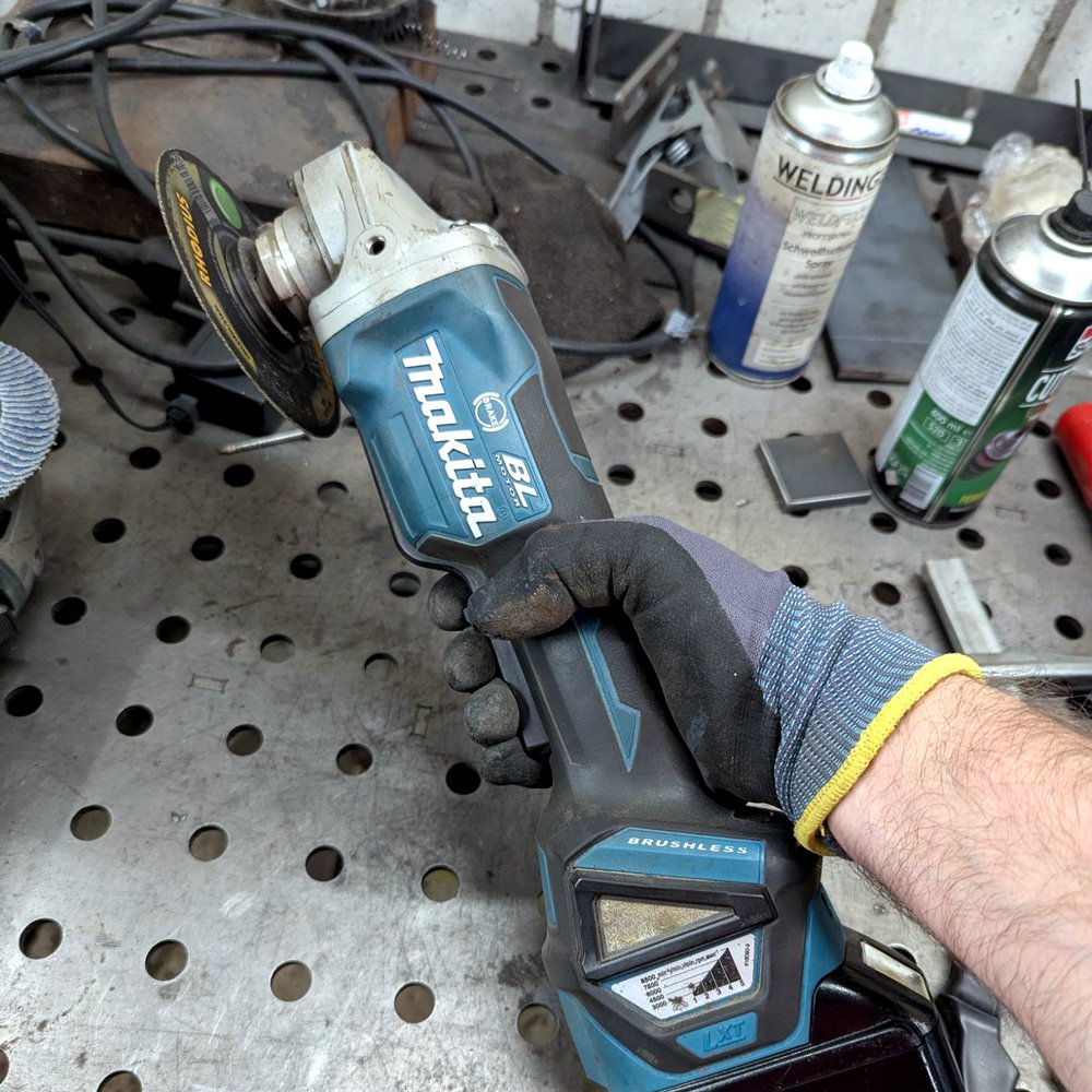 Makita DGA517 Akku-Winkelschleifer in der Hand, Werkstatt im Hintergrund